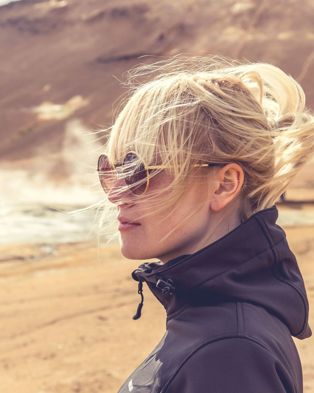 Person with sunglasses and hair blowing in the wind against a natural background
