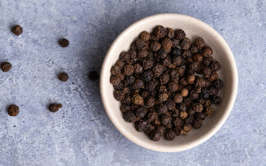A bole of black pepper on a grey background