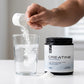 Creatine monohydrate bottle with a hand adding a scoop of powder into a glass of water