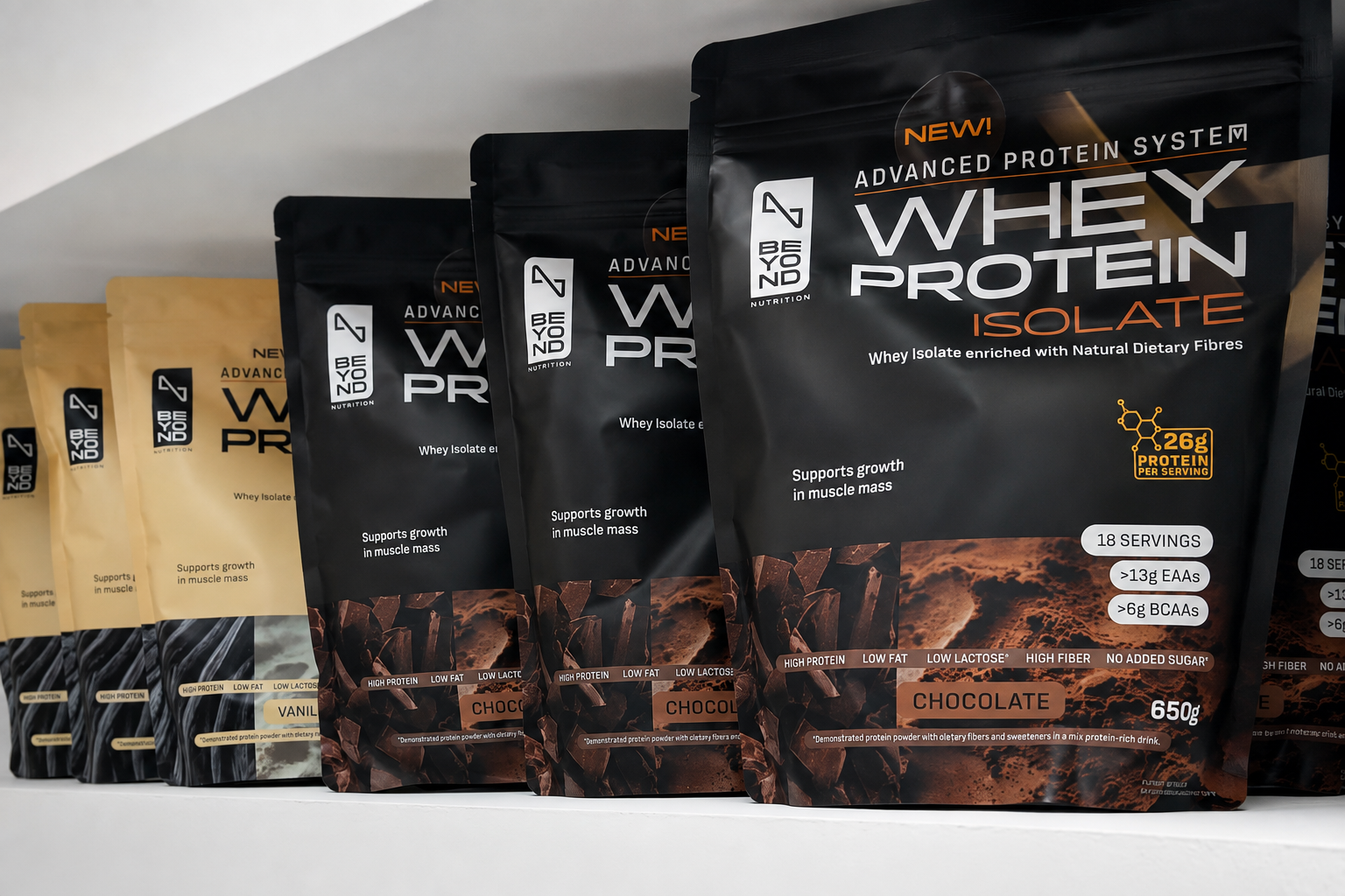 A row of Beyond Nutrition protein powder pouches on a white shelf, with the front bag prominently showing a large black pouch labeled 'Whey Protein Isolate' in chocolate flavor, alongside smaller tan and dark gray bags.