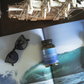 Bottle of 'RECOVER' supplement on a magazine with sunglasses and a model airplane.