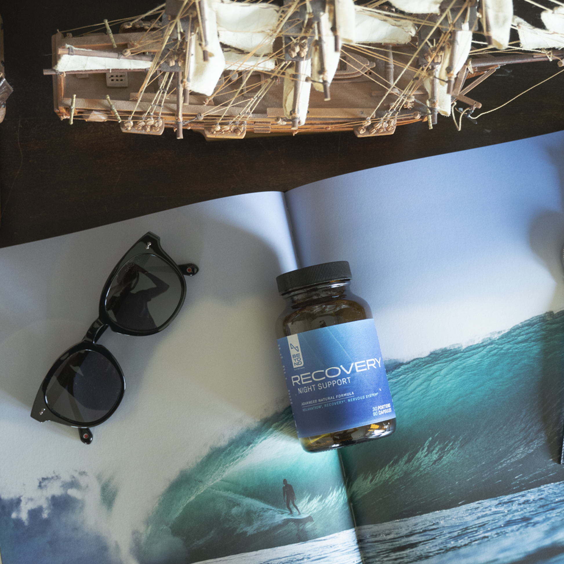 Bottle of 'RECOVER' supplement on a magazine with sunglasses and a model airplane.