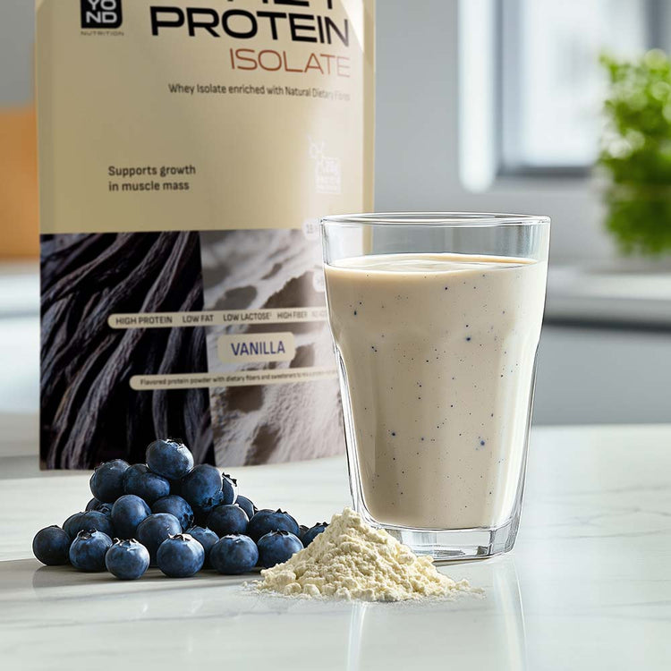 Glass of protein shake with vanilla protein powder, blueberries, and a container of protein isolate on a white surface.