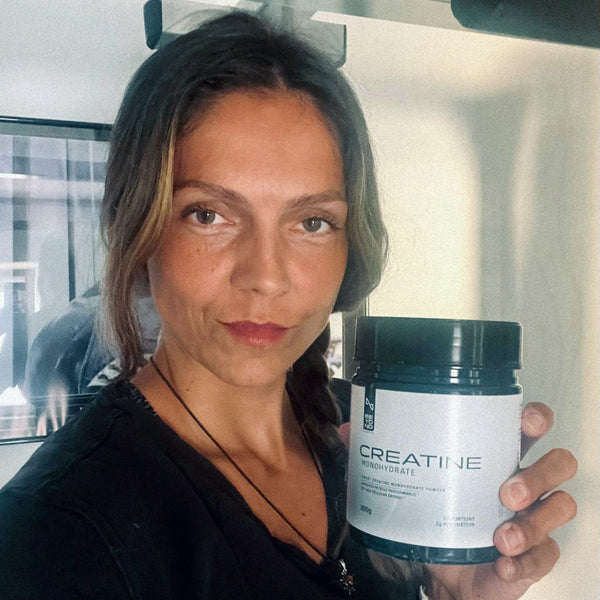 Woman holding a container labeled 'Creatine Monohydrate' in an indoor setting.