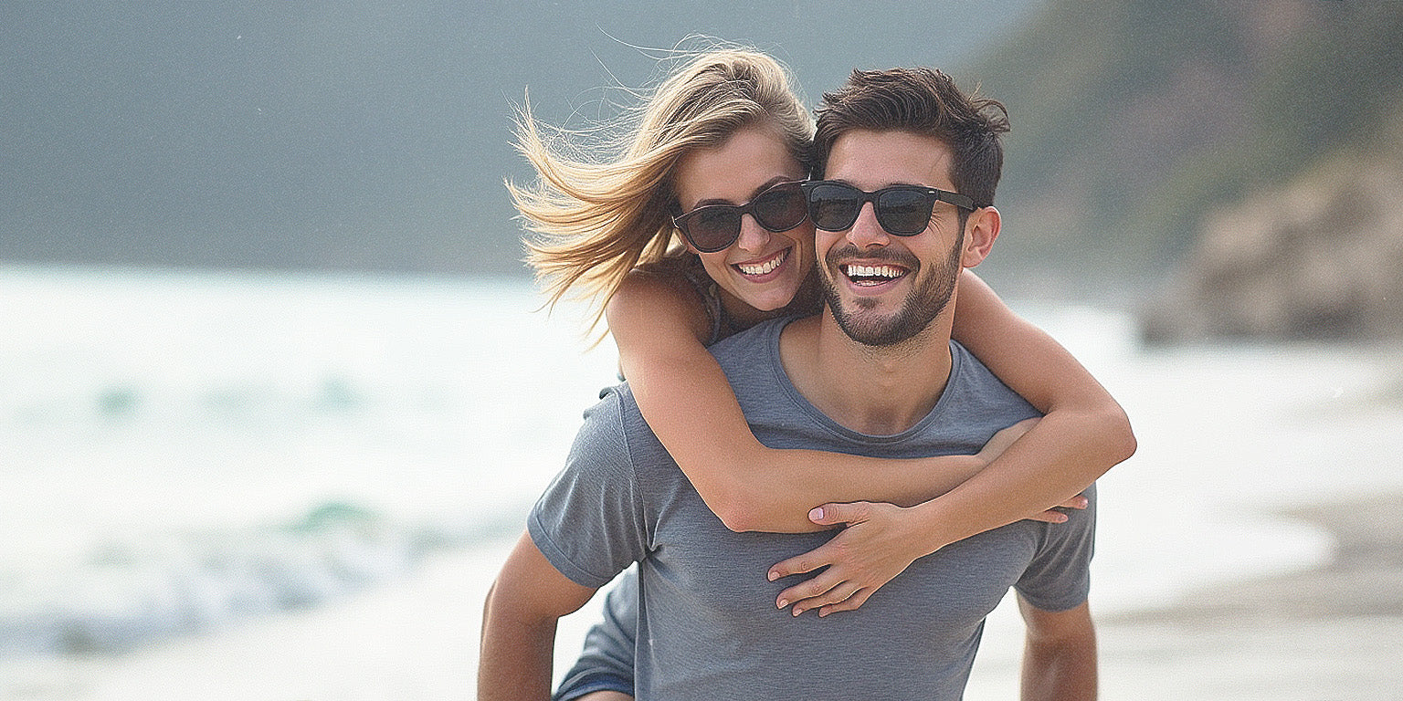 Woman hugging man from behind on the beach while both are happy and laughing