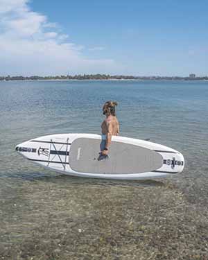 Person standing on a paddleboard in shallow water with a clear sky.